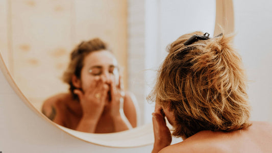 Person som tvättar ansiktet framför spegeln, illustrerar rengöring av huden efter microneedling-behandling.