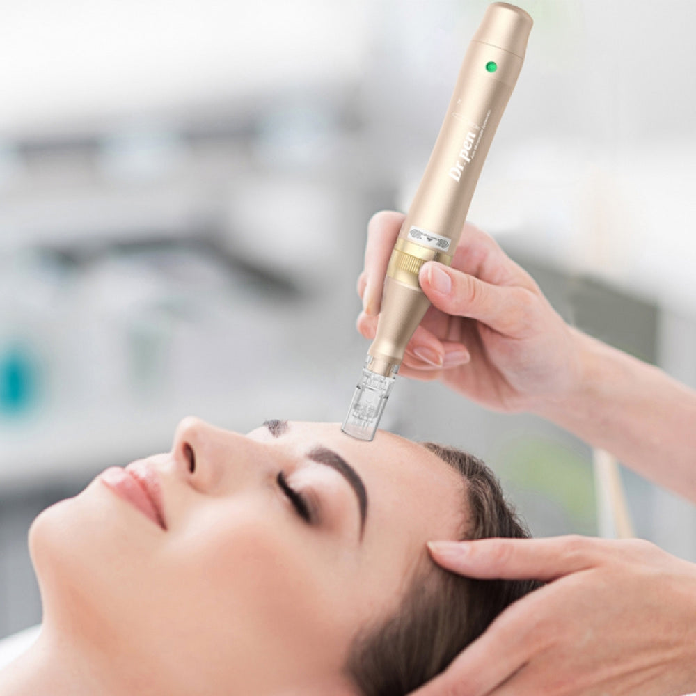 En person ligger avslappnad medan en behandlare utför microneedling i pannan med en guld-färgad Dr. Pen M5. Behandlaren håller pennan med båda händer för precision.